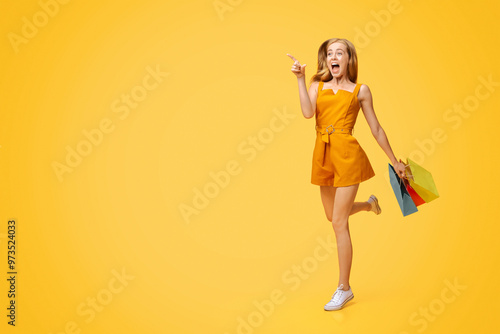 Big Sales. Excited Young Woman Running With Shopping Bags And Pointing At Free Space Over Yellow Background