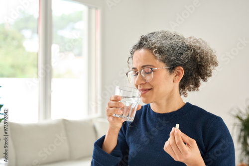 Tableau sur toile Happy healthy woman of middle age talking pill holding glass of water standing at home
