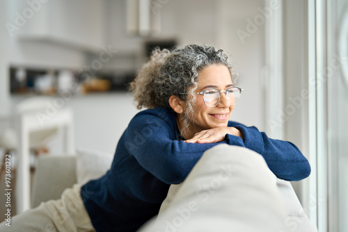 Bild auf Leinwand Happy middle aged woman sitting on comfy sofa in living room at home looking through window