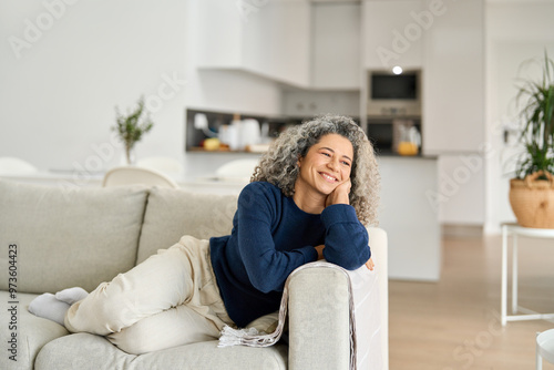 Fotografie Happy relaxed 50 years old woman laying on sofa at home looking away