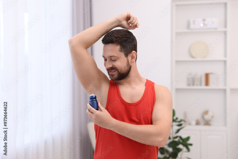 Smiling man applying roll-on deodorant at home Smiling man applying roll-on deodorant at home