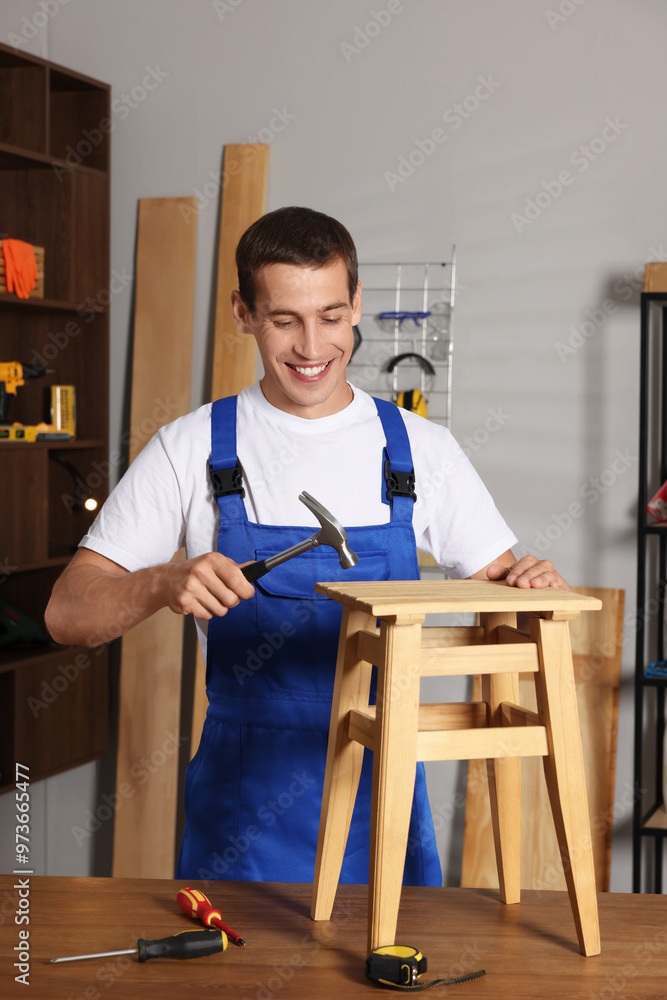 Man repairing wooden stool with hammer indoors Man repairing wooden stool with hammer indoors