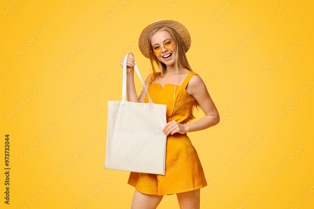 Fototapeta premium Blank Tote Bag In Hands Of Smiling Young Girl In Summer Clothes Standing Over Yellow Background, Mockup For Your Design, Copy Space