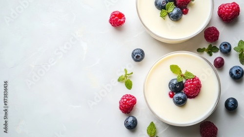 Two bowls of creamy vanilla pudding topped with fresh raspberries, blueberries and mint leaves on a white background. photo