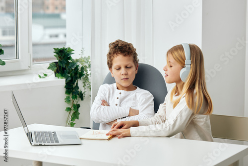 Happy brother and sister studying at home with a laptop, headphones, and tablet They are sitting at a table in the living room, fully focused and engaged in their online elearning lesson They both