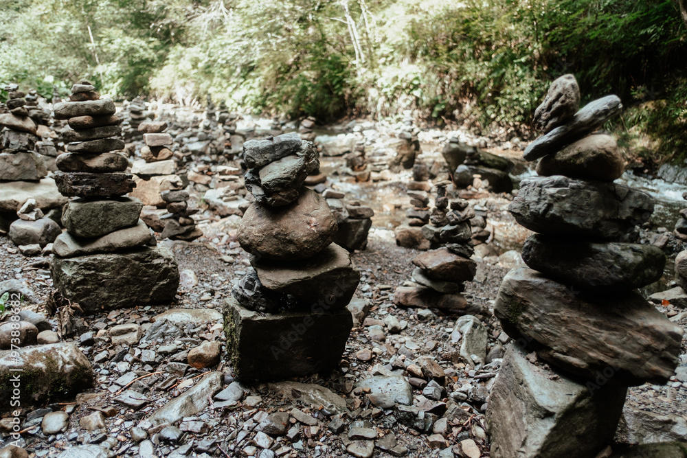Stacked stones create a tranquil landscape in a forested area near a rocky riverbank at midday Stacked stones create a tranquil landscape in a forested area near a rocky riverbank at midday