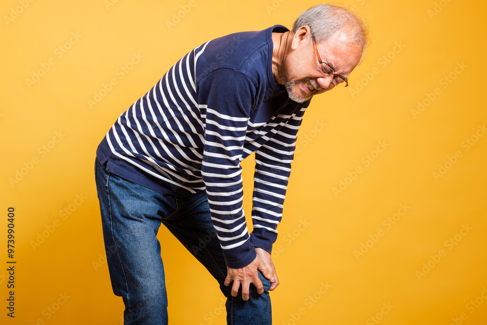 Portrait Asian old man with glasses hand holding knee joint pain studio shot isolated yellow background, senior man pensioner feeling pain suffering from knee bone joint problem Portrait Asian old man with glasses hand holding knee joint pain studio shot isolated yellow background, senior man pensioner feeling pain suffering from knee bone joint problem