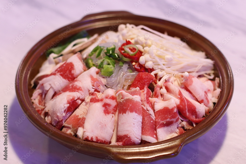A hot pot filled with thinly sliced beef bulgogi and fresh vegetables, ready to be cooked. The ingredients are arranged beautifully, preparing for a savory, warming meal. A hot pot filled with thinly sliced beef bulgogi and fresh vegetables, ready to be cooked. The ingredients are arranged beautifully, preparing for a savory, warming meal.