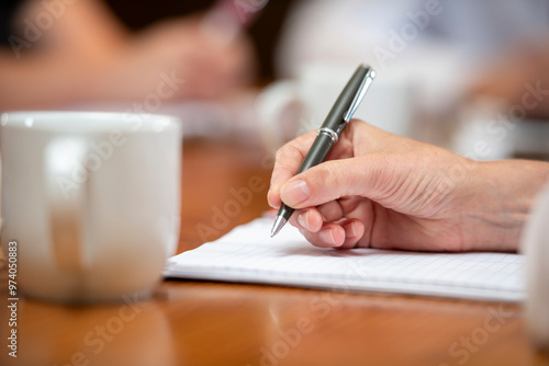 Womans hand holding a pen poised to take notes in a business mee