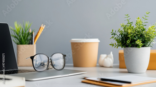 Clean and organized office desk featuring a laptop, eyeglasses, coffee cup, and green plants, creating a modern minimalist workspace.
