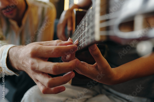 Billede på lærred Close-up of hands fretting on guitar strings while another person guides playing technique