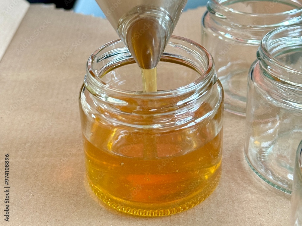 A detailed shot of honey being filled into a glass jar using a stainless steel funnel, showing the honey’s golden hue and the bottling process. A detailed shot of honey being filled into a glass jar using a stainless steel funnel, showing the honey’s golden hue and the bottling process.