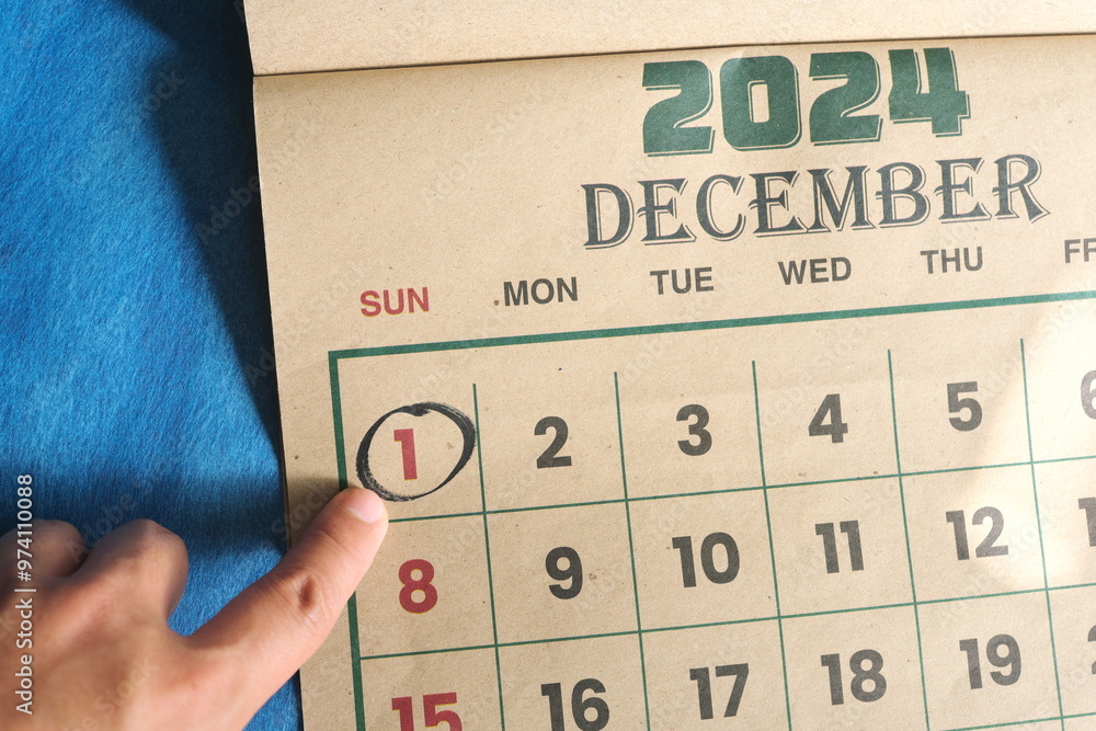 Hand pointing on December 1 2024 date on calendar flat lay in blue background. First day of the month reminder.