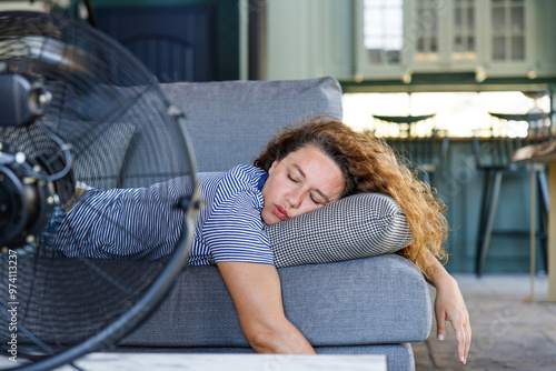 Young woman lying in front of the electric fan at home, overwhelmed by the heat