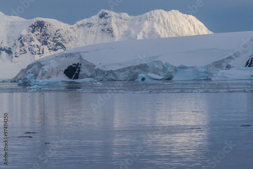 Icebergs and Glaciers align the coast of the Antarctic peninsula, and its many islands. A very tranquil sea reflects the early morning light in the Gerlache strait. photo