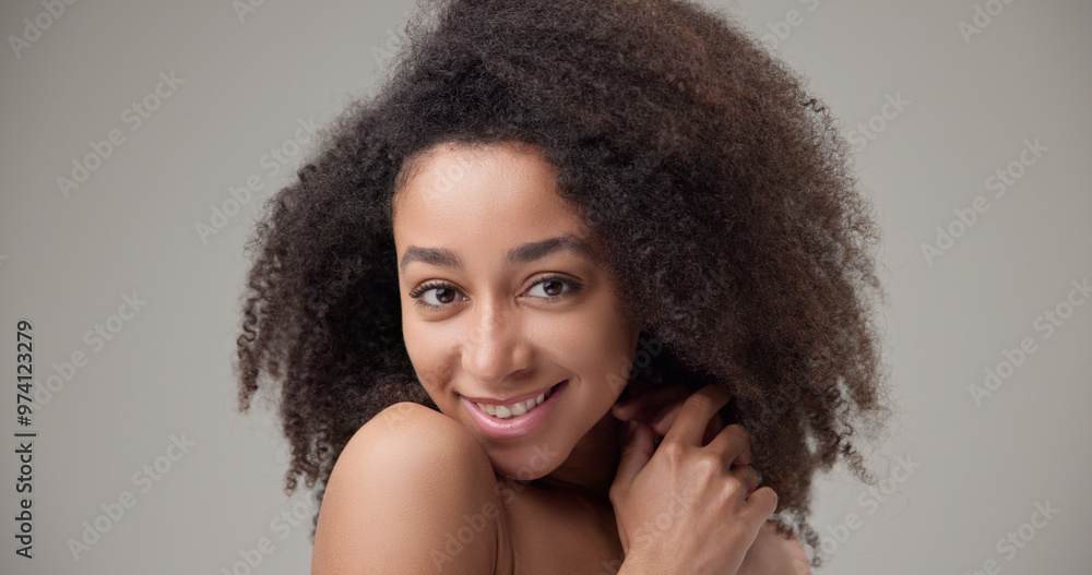 Beauty and healthcare concept - beautiful African American woman with curly afro hairstyle and clean, healthy skin touching face with hand, doing facial massage, posing and looking at camera