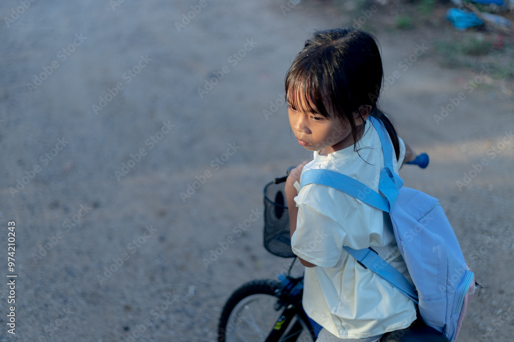 A young girl is riding a bicycle with a blue backpack on her back
