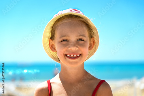 Close up of happy girl in hat ooks at camera and laughs on sandy beach with blue sea in hot summer day. Vacation travel holiday photo