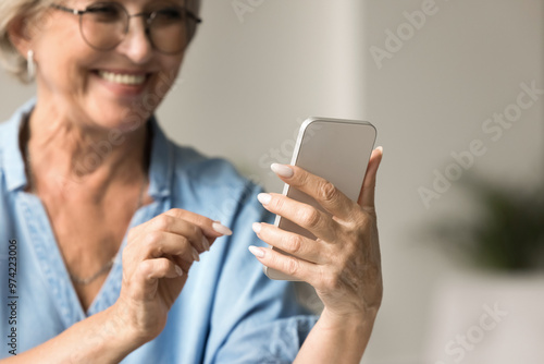 Close up happy older woman using her smartphone, typing message, choose goods, buying services, enjoy remote chat with friend or online communication, read news, check planner or organizer using app photo