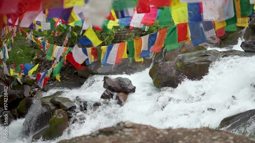 River stream flows through a rocky landscape and Buddhist prayer flags at Udaipur, Himachal Pradesh, India. 4K Beautiful summer nature landscape. Wild mountain river water splashing in summer day.