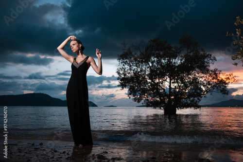 Beauty and nature. Fairy and sensual portrait of pretty young woman wearing long black dress against dramatic sky and sea view photo