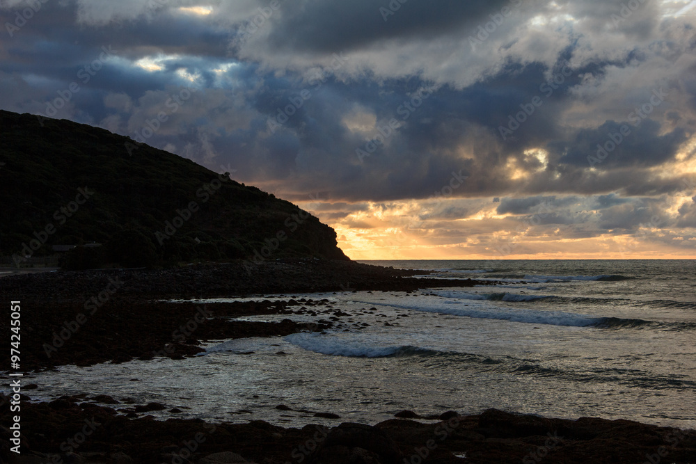 Obraz premium Dramatic sunset over rocky shore of Pacific Ocean near Raglan, New Zealand