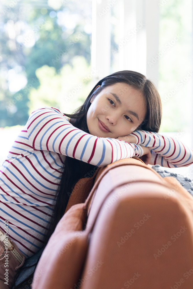 At home, Relaxing on couch, young asian woman in striped shirt smiling and daydreaming At home, Relaxing on couch, young asian woman in striped shirt smiling and daydreaming