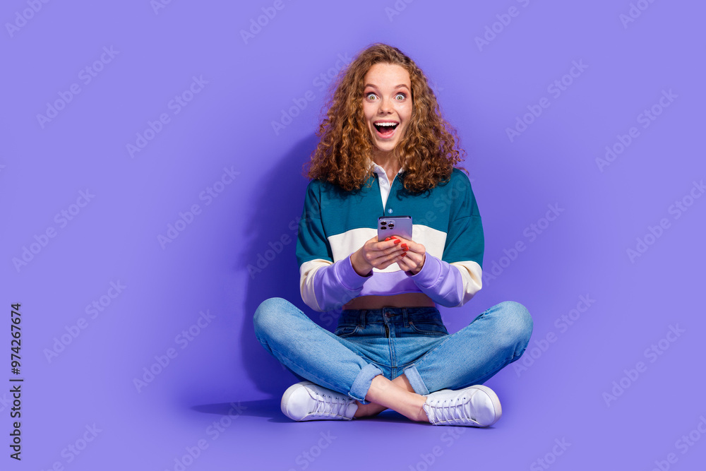 Full size photo of nice young girl sit floor hold smart phone isolated on violet color background Full size photo of nice young girl sit floor hold smart phone isolated on violet color background