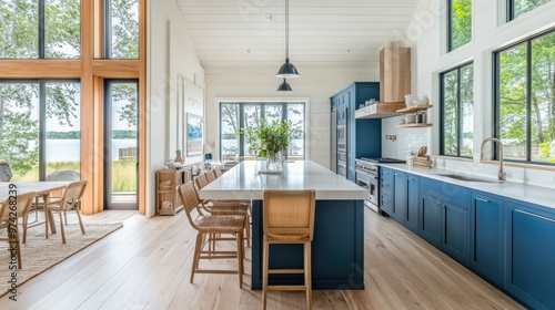 Fototapeta Naklejka Na Ścianę i Meble -  Modern kitchen with blue cabinets, white countertop, and large windows overlooking a lake.
