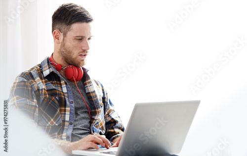 Man, headphones and typing with laptop for music software, audio or content creation at home. Young, male person or musical artist with headset on computer for digital sound track, app or podcast