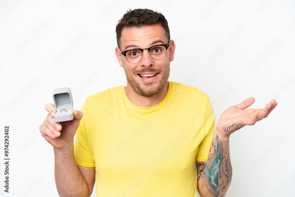 Young caucasian man holding a engagement ring isolated on white background with shocked facial expression Young caucasian man holding a engagement ring isolated on white background with shocked facial expression