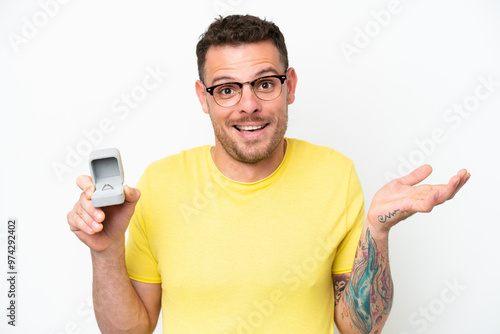 Young caucasian man holding a engagement ring isolated on white background with shocked facial expression