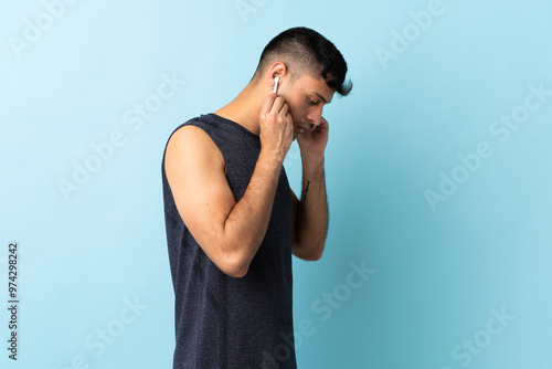 Young Colombian man isolated on blue background listening music