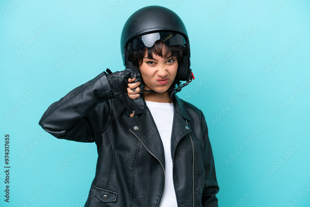 Young Argentinian woman with a motorcycle helmet isolated on blue background showing thumb down with negative expression Young Argentinian woman with a motorcycle helmet isolated on blue background showing thumb down with negative expression
