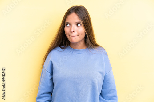 Young caucasian woman isolated on yellow background having doubts while looking up