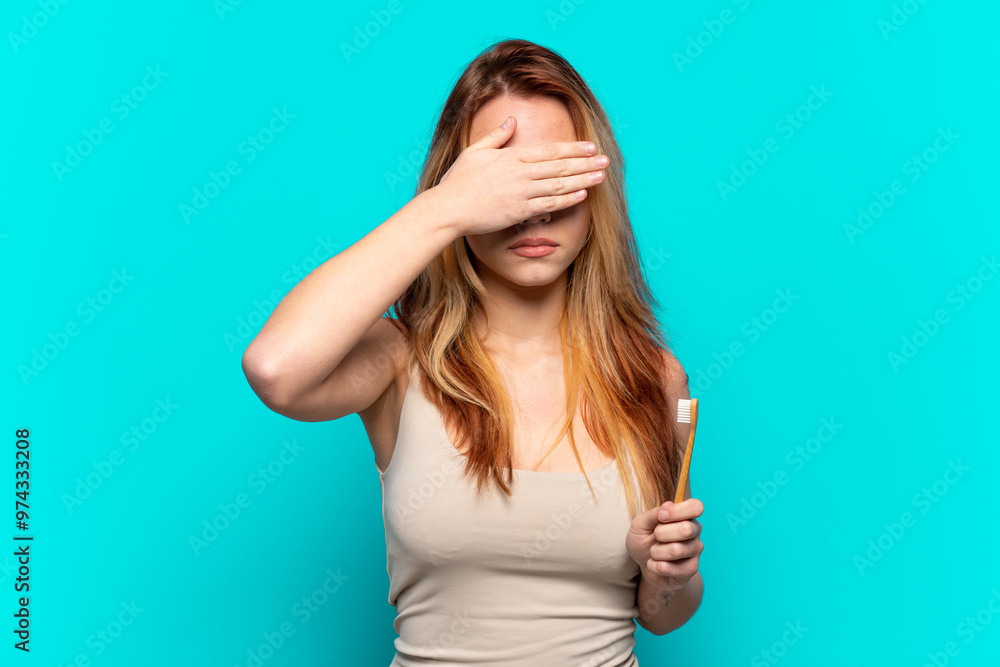 Teenager girl brushing teeth over isolated blue background covering eyes by hands. Do not want to see something Teenager girl brushing teeth over isolated blue background covering eyes by hands. Do not want to see something