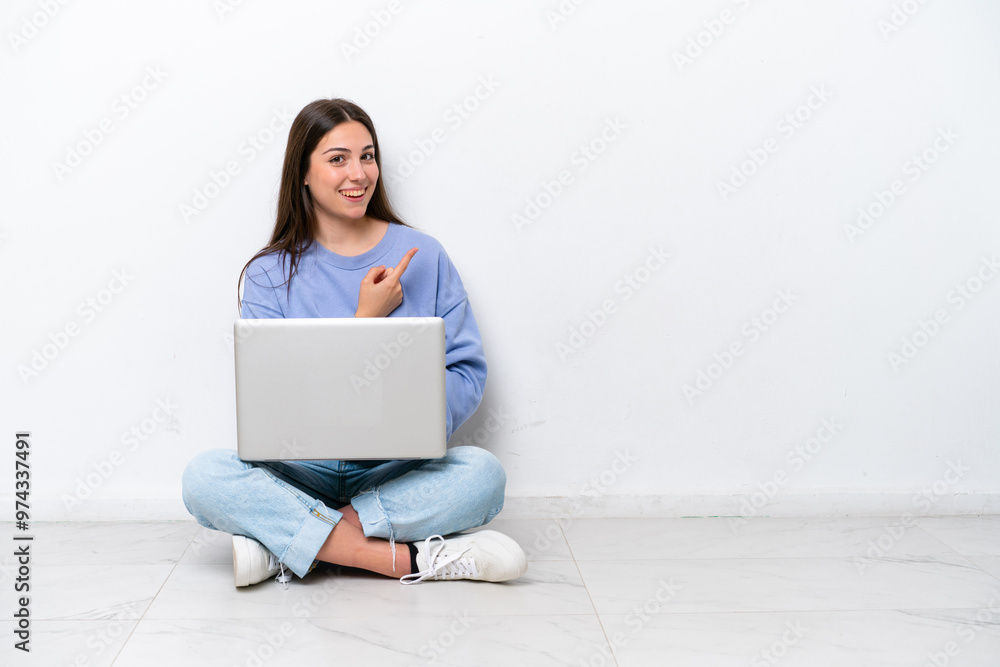Young caucasian woman with laptop sitting on the floor isolated on white background pointing to the side to present a product Young caucasian woman with laptop sitting on the floor isolated on white background pointing to the side to present a product