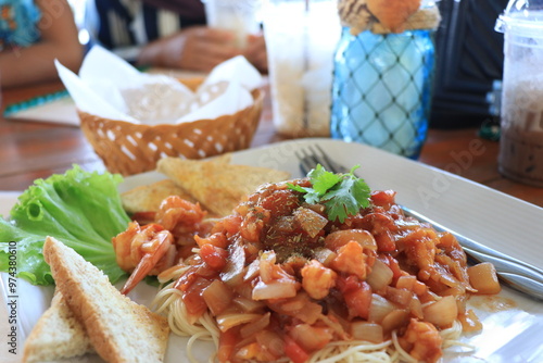 A plate of spaghetti with shrimp, tomato sauce, and garlic bread.