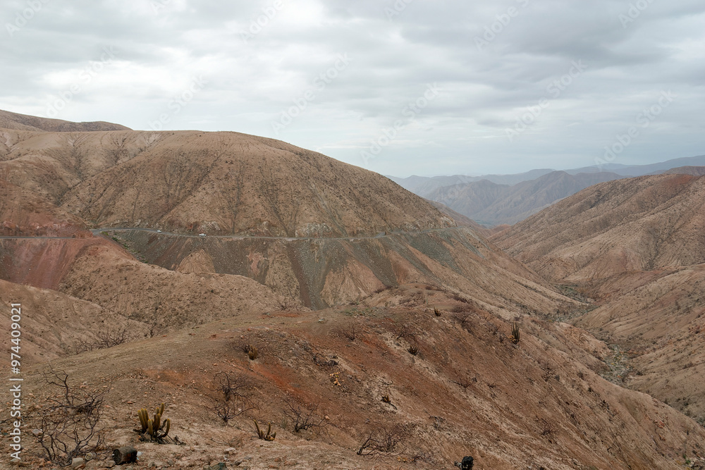 Cars driving on a winding mountain road through a barren desert landscape under overcast skies, capturing adventure and exploration in the arid wilderness of a canyon Cars driving on a winding mountain road through a barren desert landscape under overcast skies, capturing adventure and exploration in the arid wilderness of a canyon