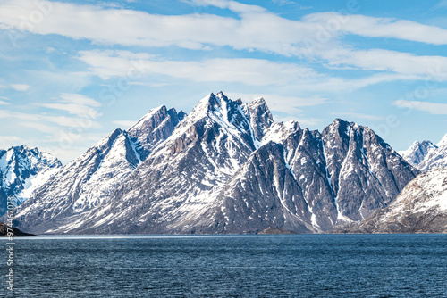 Snow-capped jagged mountains by the sea under a blue sky, scenic Arctic landscape, Greenland fjord