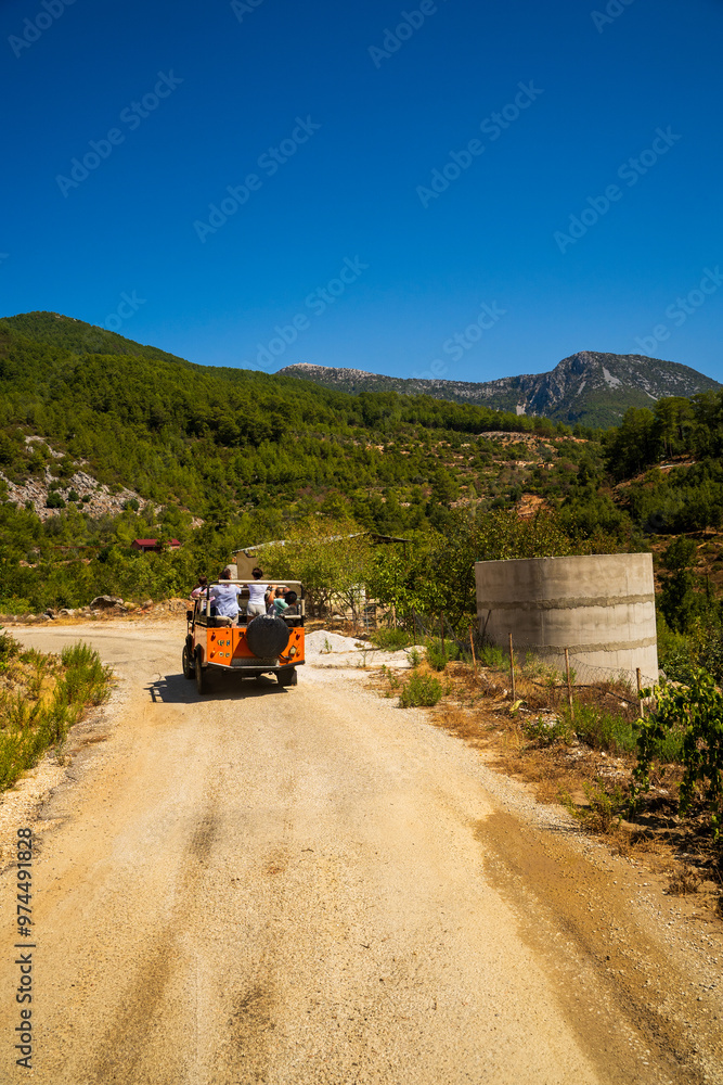 A vibrant jeep tour navigates a rural path in Antalya, Turkey, showcasing stunning mountain views under a clear blue sky, capturing the essence of outdoor exploration and adventure.