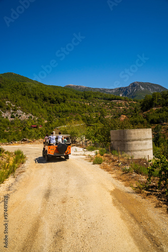 Obraz na płótnie A vibrant jeep tour navigates a rural path in Antalya, Turkey, showcasing stunning mountain views under a clear blue sky, capturing the essence of outdoor exploration and adventure. w salonie