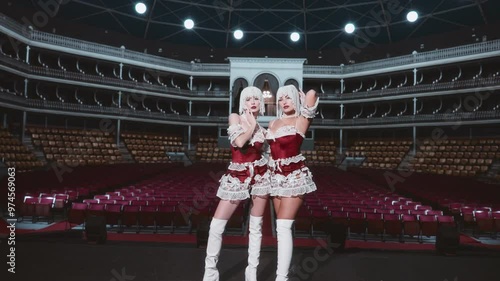 Two performers in red and white costumes stand confidently on an empty stage, illuminated by spotlights, capturing the allure and excitement of a captivating show. photo