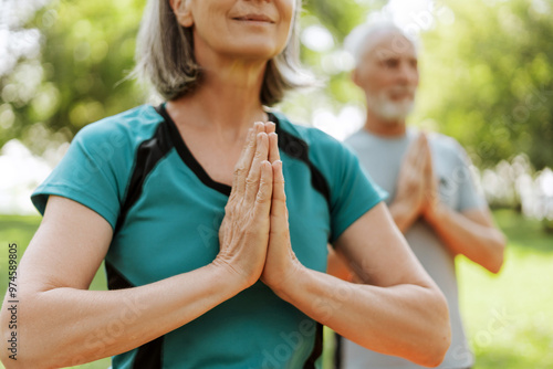 Senior couple practicing yoga together outdoors in the park selective focus on hands