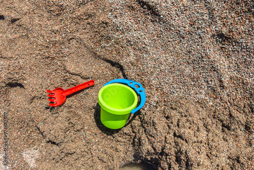 A children's green plastic bucket and rake on a sandy beach. Vacation at sea.