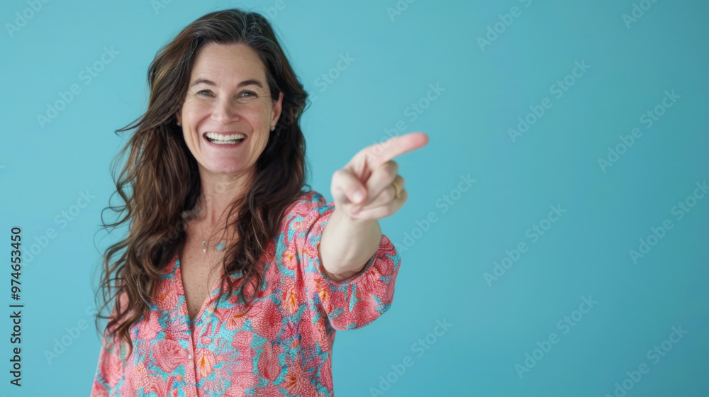 Smiling woman with long wavy hair points to the right against a light blue background in a casual setting Smiling woman with long wavy hair points to the right against a light blue background in a casual setting