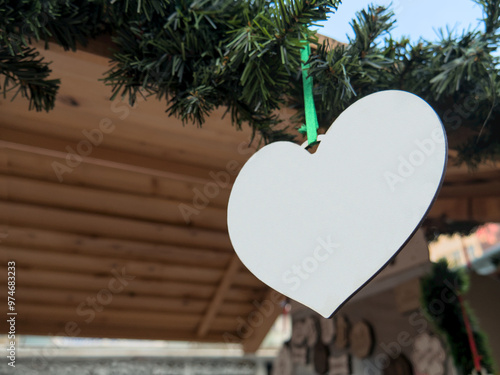 White heart-shaped wooden tile hanging on a Christmas garland on the roof of a street wooden stall selling Christmas decoration. Template, mockup, copy space photo