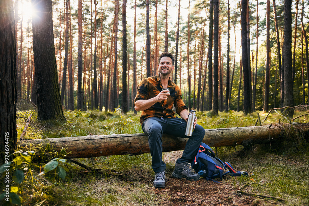 Adult man resting in forest during autumn hike drinking from thermos Adult man resting in forest during autumn hike drinking from thermos