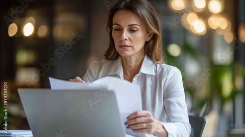 Busy 40-Year-Old Business Woman Working in Office, Reviewing Documents, Financial Reports, and Tax Invoices. Mid-Aged Accounting Manager, Executive or Lawyer Using Laptop to Check Paper Files and Mana