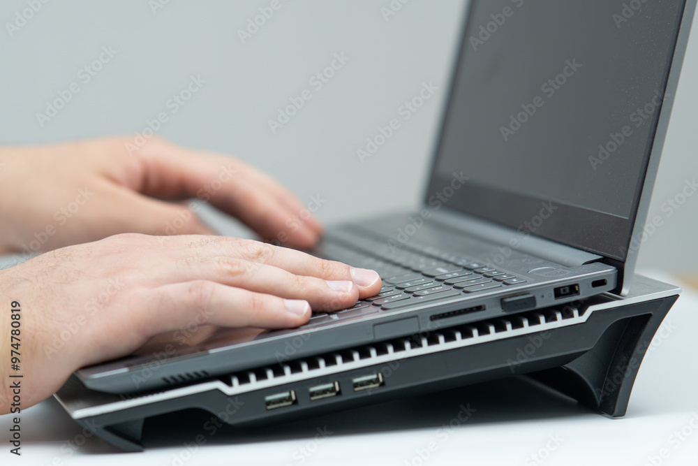 Close up of male hand using laptop standing on cooling stand Close up of male hand using laptop standing on cooling stand